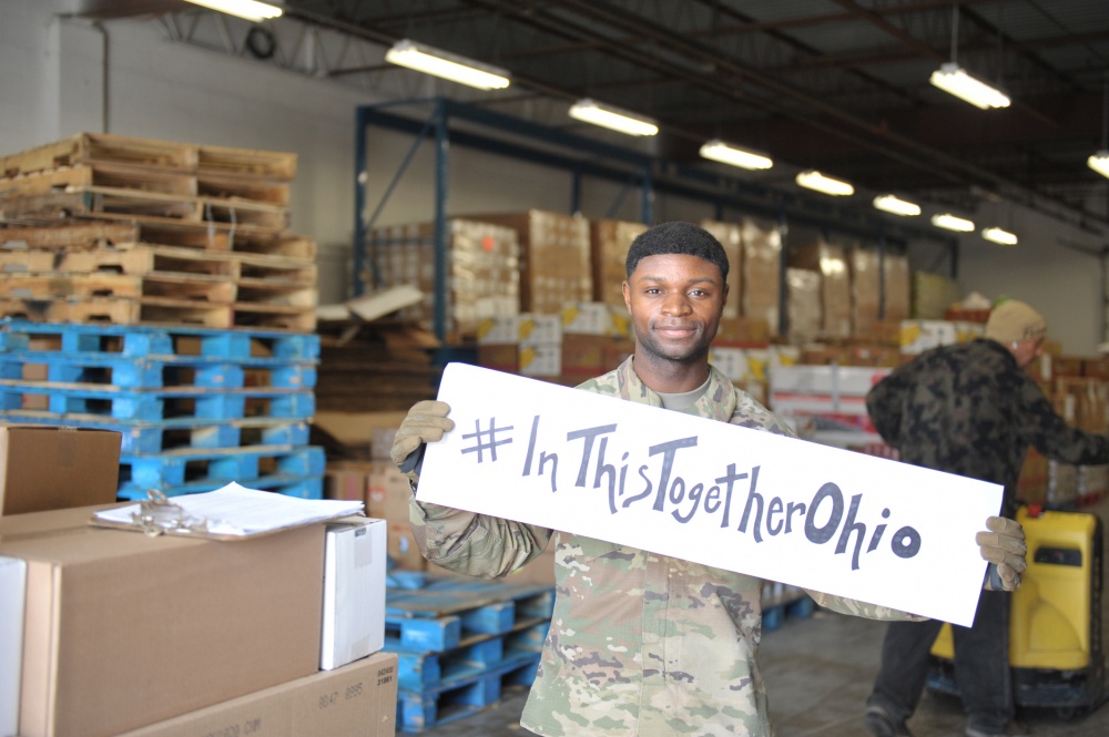 Soldier holds #InThisTogetherOhio sign in warehouse.