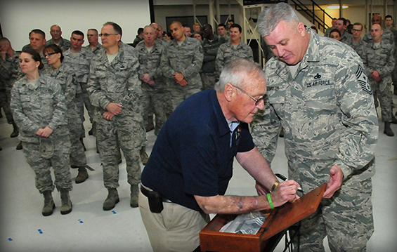 Former 178th Wing command chief Orrin Grosjean signs his name on a heritage box while outgoing wing command chief, Chief Master Sgt. Ottis LeMaster, looks on.