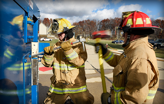 Staff Sgt. Andrew Burton (right), a firefighter with the 180th Fighter Wing, slams the striking edge of his axe into a Halligan bar held by Senior Airman William Echols.