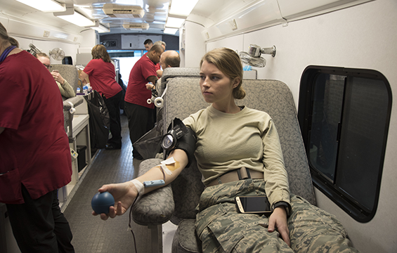 Close up of female Airman with other members in additional bays donating blood on mobile unit.