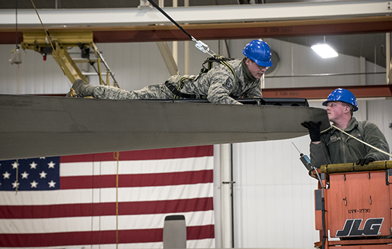 Closeup of airmen on top of aircraft wing and on lift.