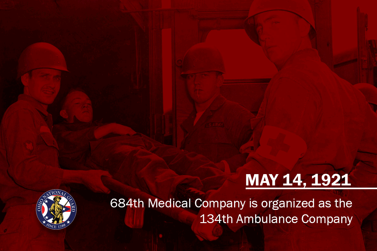 The photo shows members of Company A, 112th Medical Battalion loading a simulated casualty into an ambulance during annual training, circa 1960.