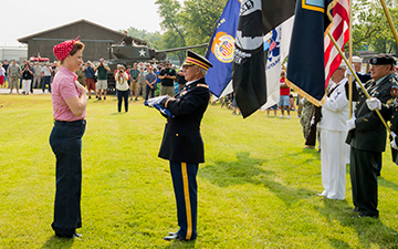 Dressed as “Rosie the Riveter,” Dawn Rumbutis (left) delivers the colors to the commander of color guard