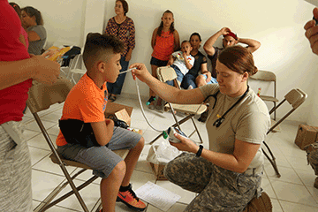 Spc. Tarrah Berg, a medic with the 285th Medical Company (Area Support), takes the temperature of a child.