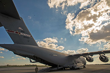 An Airman guides an Ohio Army National Guard Humvee onto a C-17 Globemaster III from back of plane.