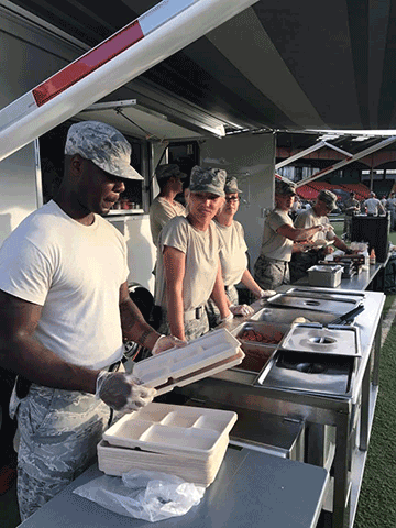Airmen standing behind food warmer line ready to serve.