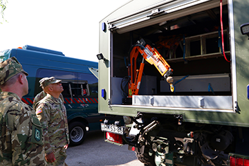 Soldiers, looking at robotic type arm in back of open truck.
