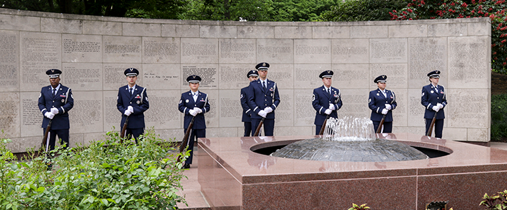 Airman honor guard stand in formation in fron to f wall monument with fountain in front.