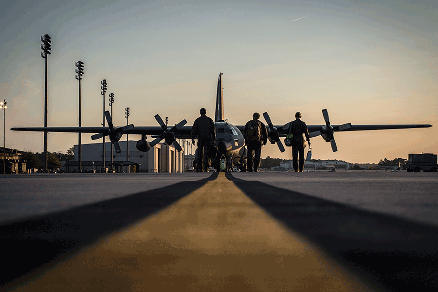 Loadmasters walk toward C-130H Hercules in early morning sun.