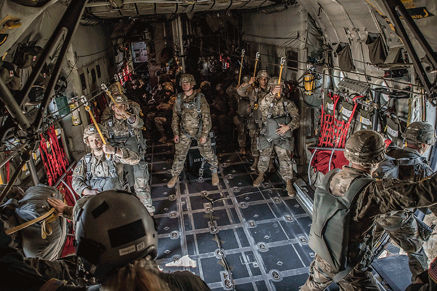 Paratroopers tethered inside open C-130H Hercules preparing for jump.
