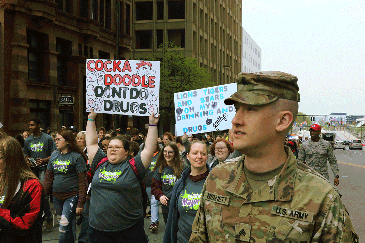 Soldier marches in parade with kids for WE ARE THE MAJORITY RALLY. Kids carry signs reading: 'COCKA DOODLE DONT DO DRUGS' and 'LIONS TIGERS AND BEARS ON MY, DRINKING AND DRUGS GOODBYE!'