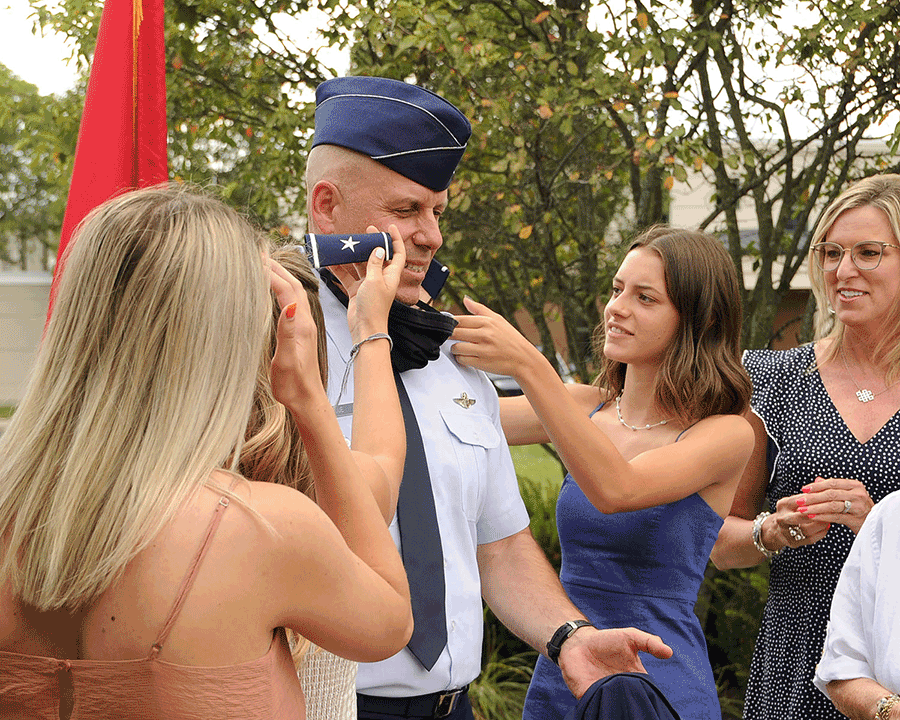 Family members affix new one-star shoulder boards on the epaulets of officer's uniform shirt.