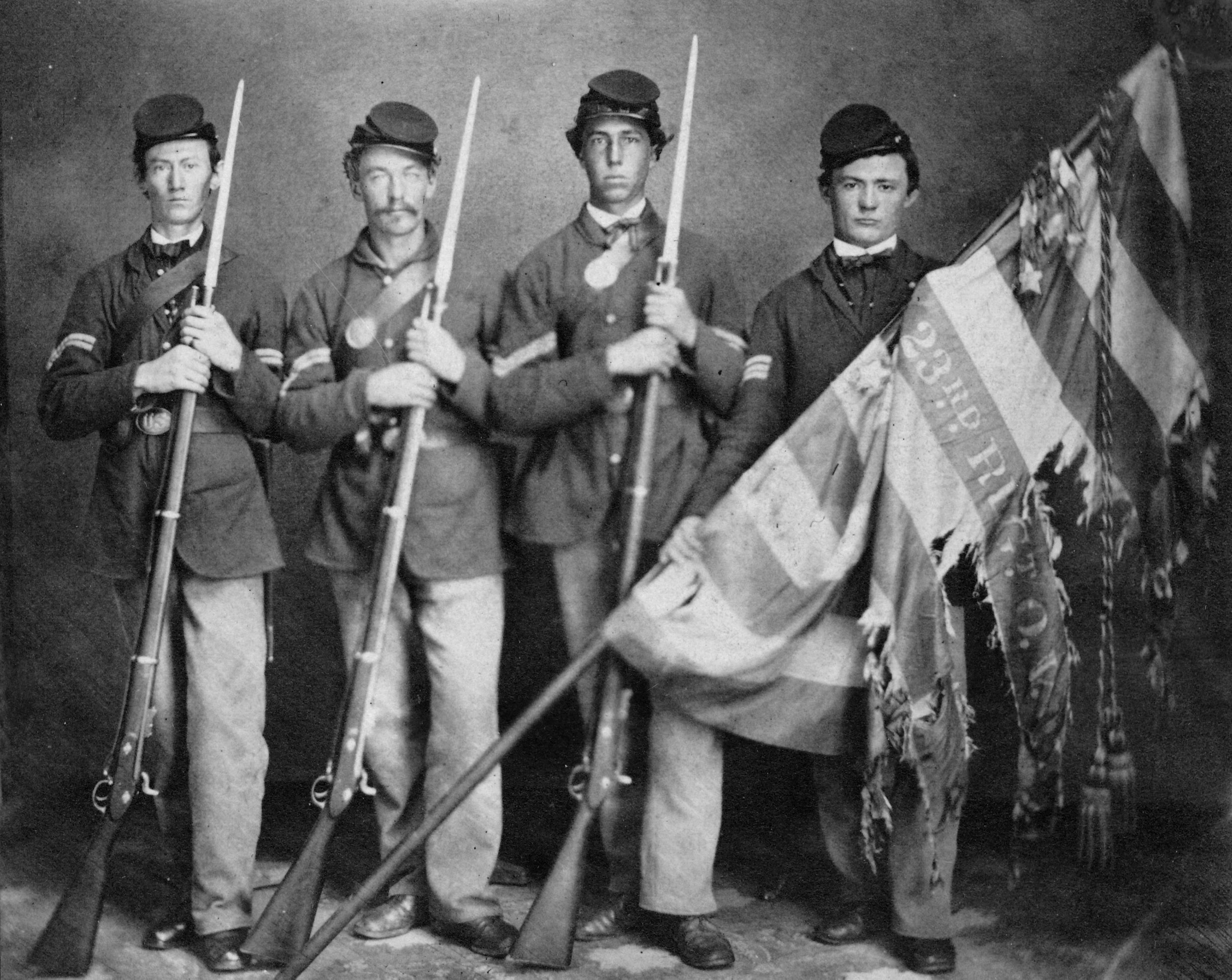 Black and white photo of 4 Soldiers posing with tattered flag