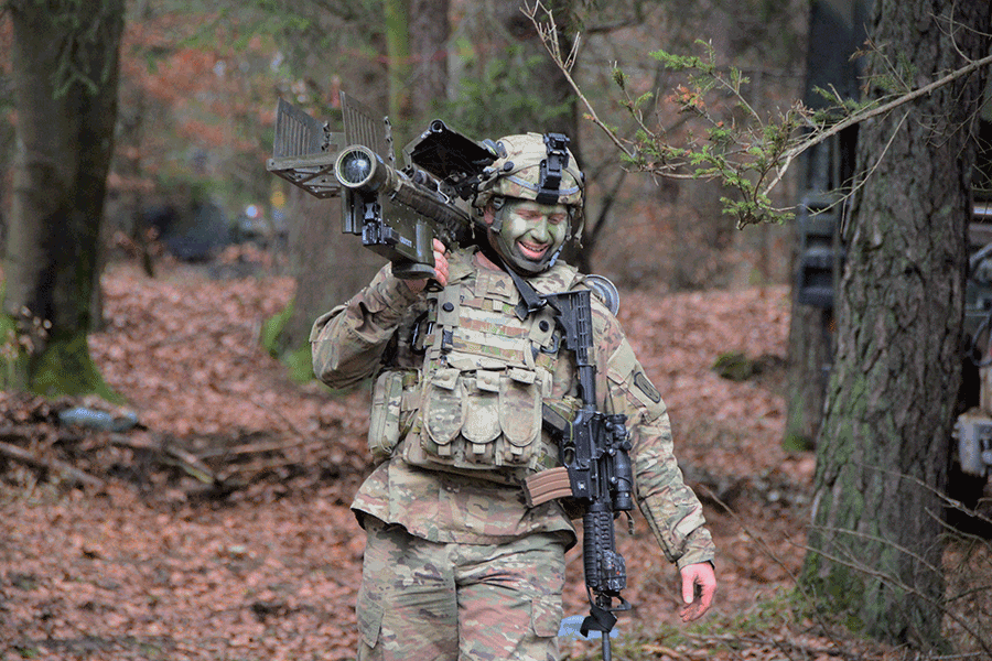 Soldier comes out of woods with weapon on his shoulder.