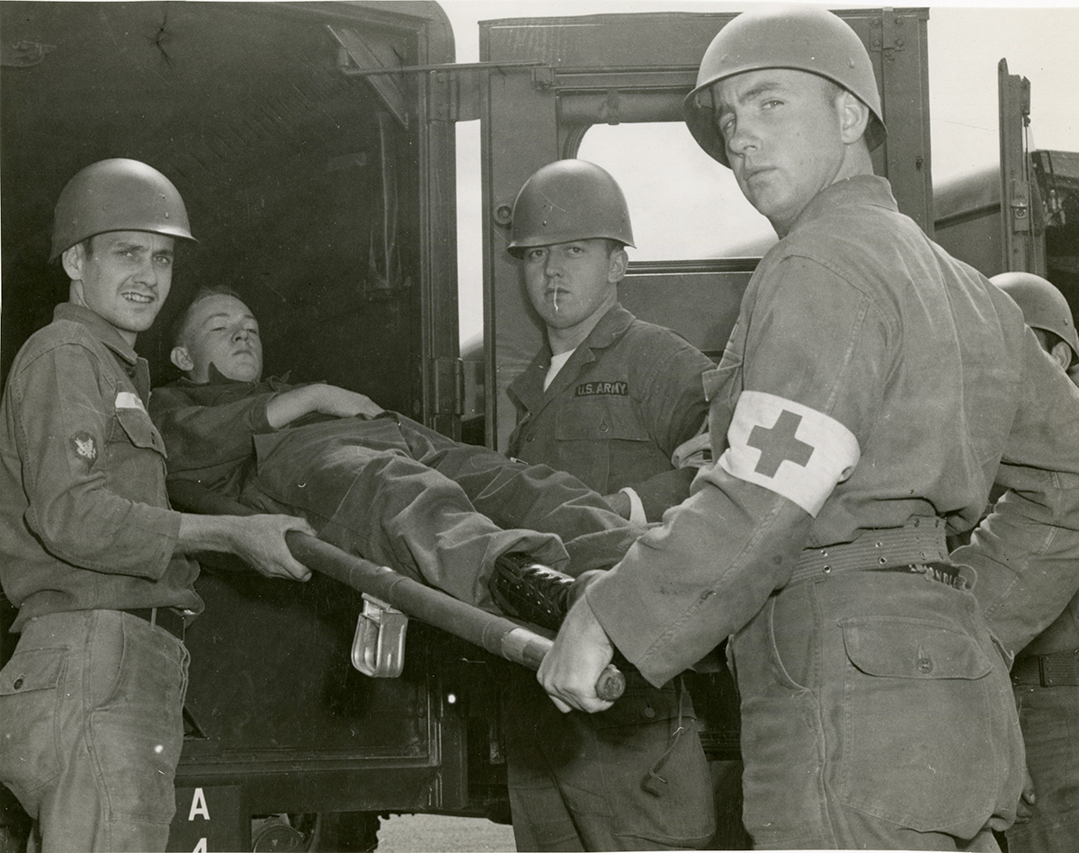black and white photo of Soliders loading man on stretcher into back of a vehicle