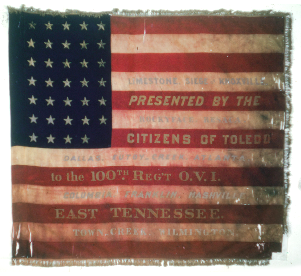 Square distressed flag with battle commmorated in red white stripes.