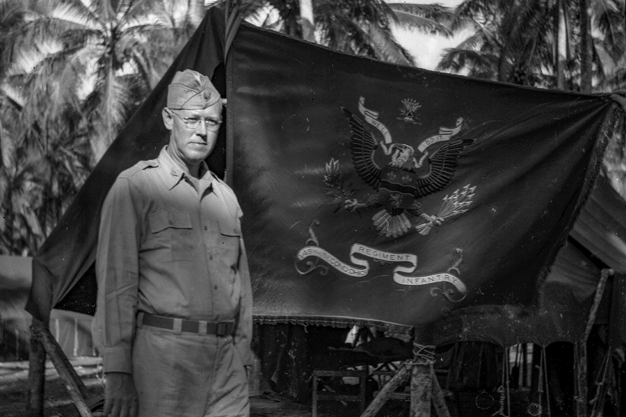 Colonel poses with flag outside tent