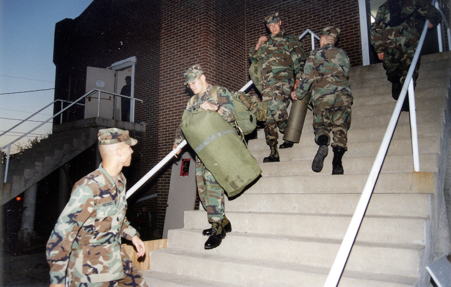 Soldiers carry their gear down stairs of armory.