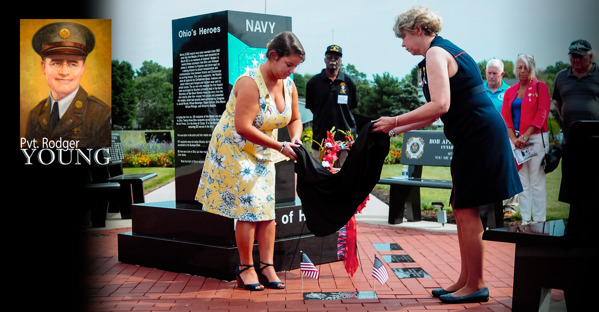 Women uncover plaque on ground at memorial with inset of Pvt. Rodger Young