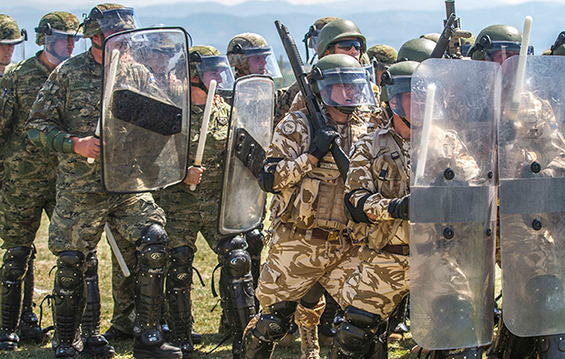 Romanian and Croatian soldiers, outfitted in riot gear, prepare to go through the evaluation lane for non-lethal systems training.
