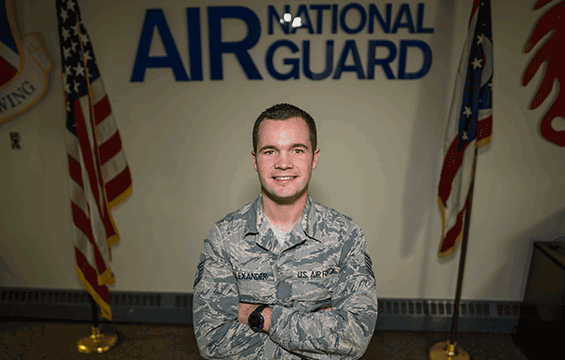 Air Guard member in uniform in front of flags.
