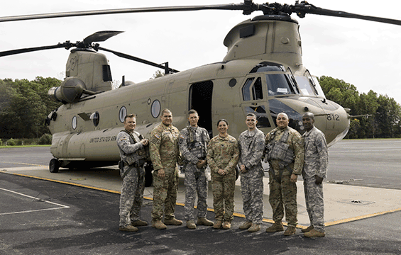 Soldiers stand in front of chinook helicopter.