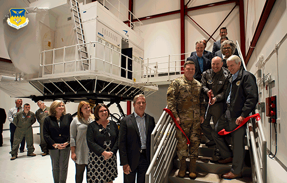 group on base of stairs to simulator cutting a red ribbon with staff on floor watching.