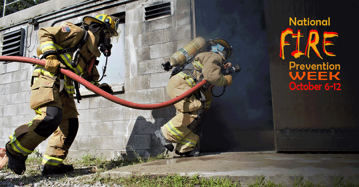 Firefighters from the 180th Fighter Wing take hose into a smoke-filled building.