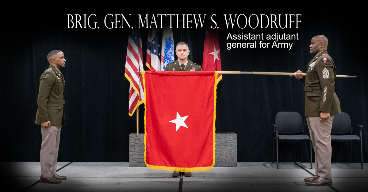 Woodruff standing at podium while  one-star flag is unfurled.