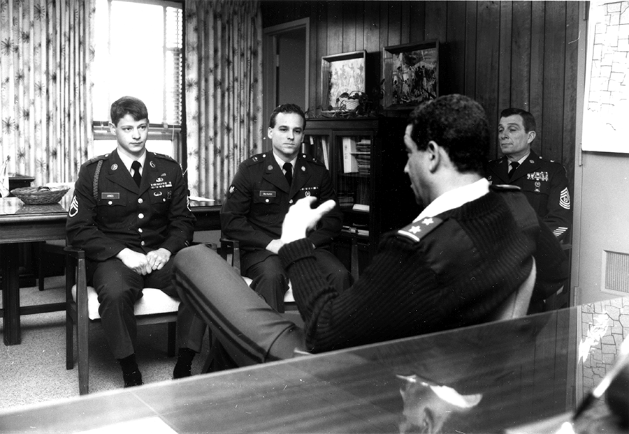 Black and white photo of NCO Jones sitting in office with Commanders.