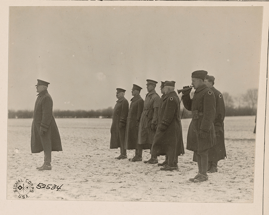 cepia-tone of General stands facing left in front of row of Soldiers in snow covered field.