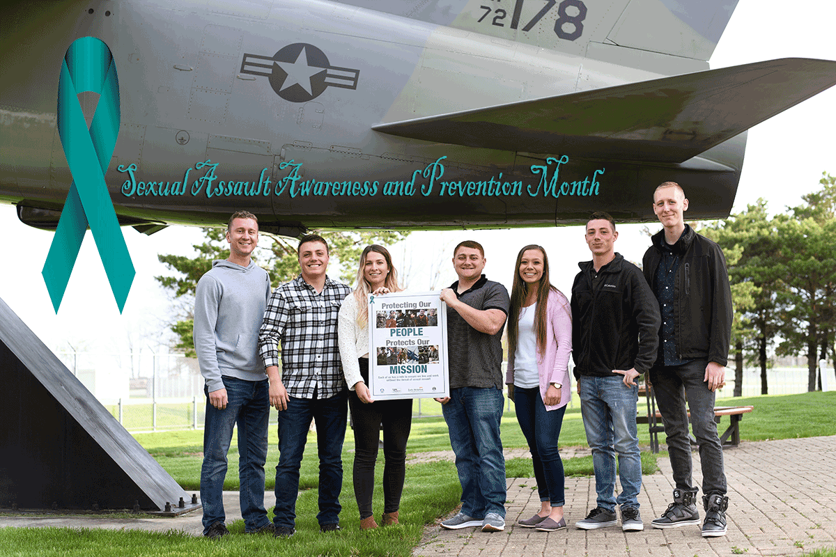 Airmen pose with SAAP poster under aircraft.