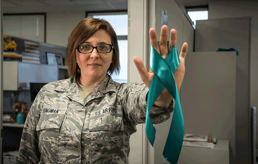 Female in Airman camo holds up teal ribbon for Sexual Assault Awareness in her office