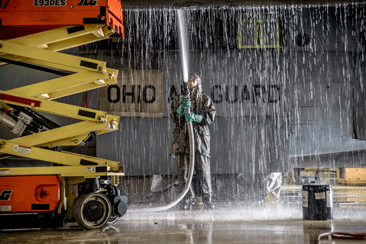 Airman in raingear with water pouring down on from washing aircraft.