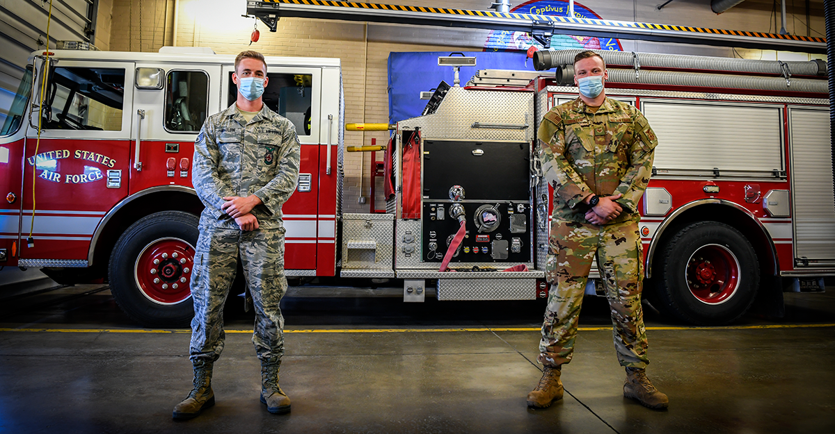 Airmen stand in front of firetruck.