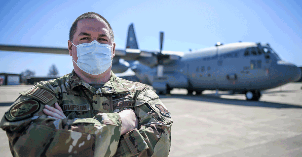 Male Airman poses with mask in front of aircraft.