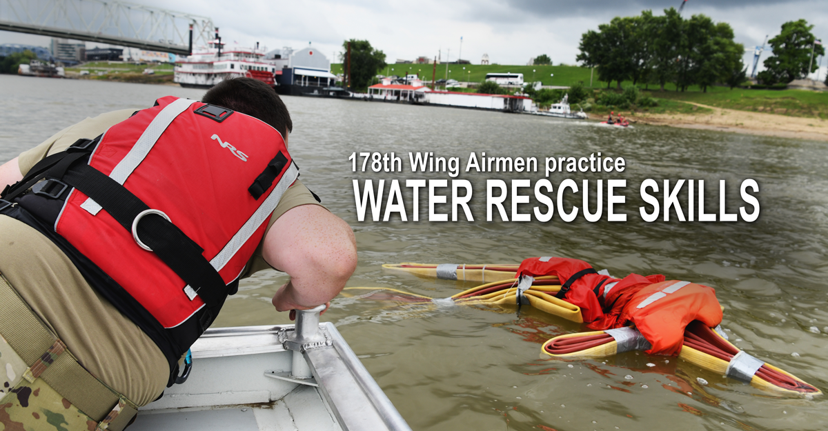 Airman hangs on side of watercraft to retrieve simulated body in water.