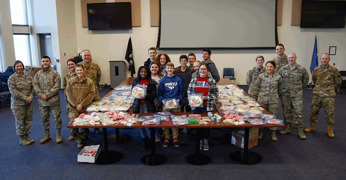 Students and Airmen stand around tables of cookies