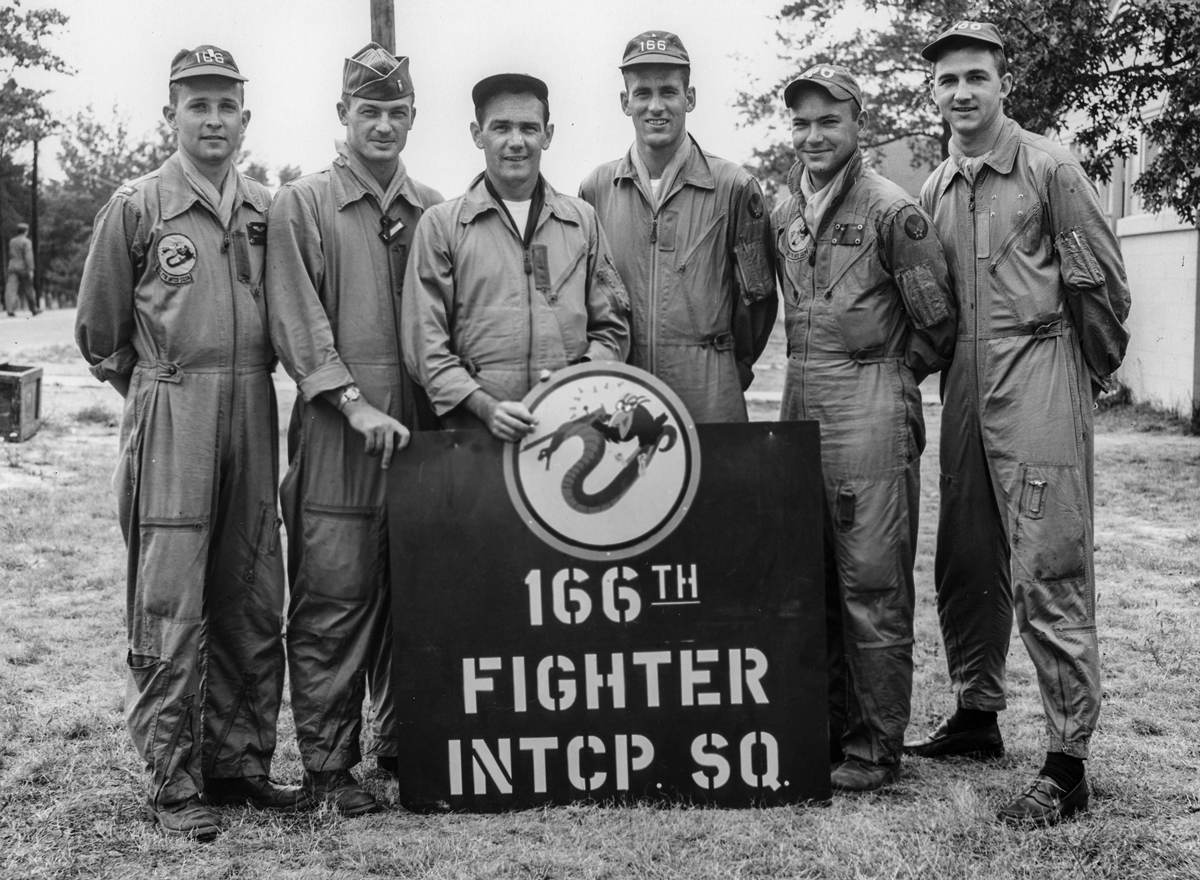  Black and white photo of 6 pilots around banner. 