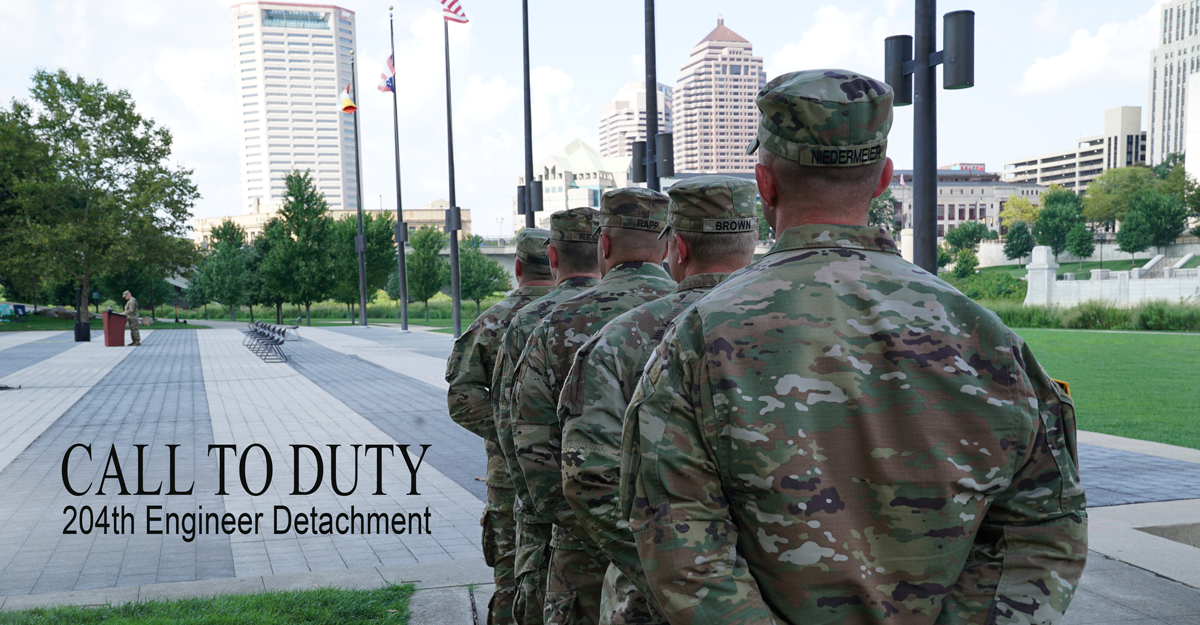 Soldiers stand at attention facing Columbus skyline.