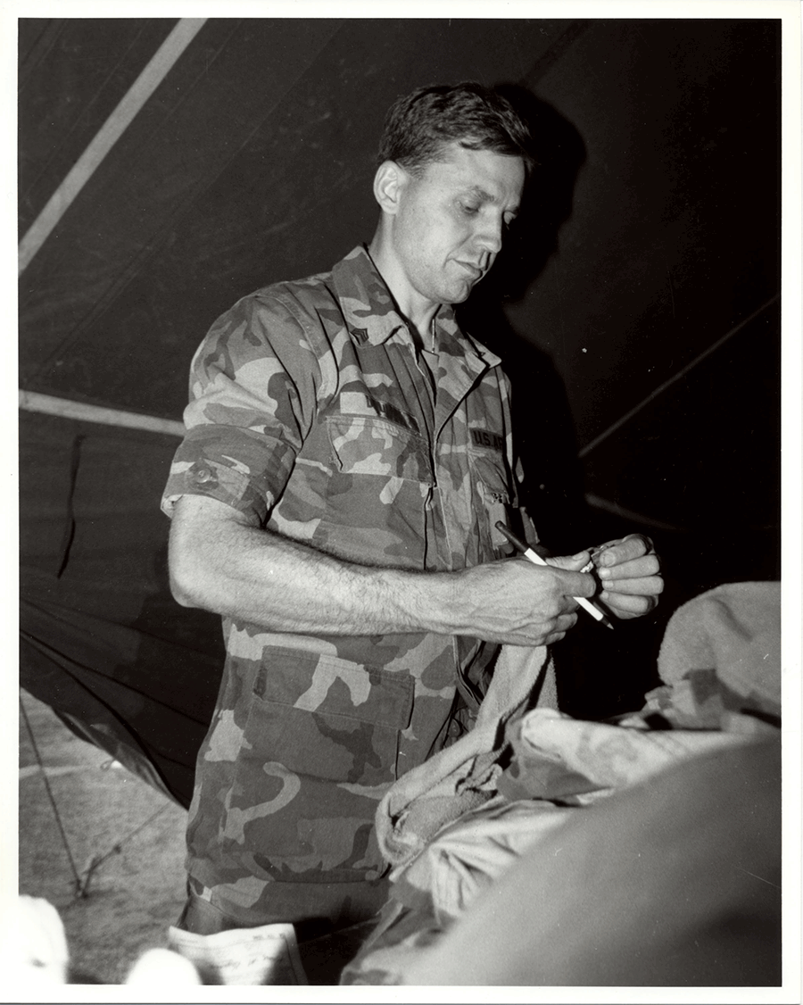 Black and white photo of Soldier in camo standing inside tent. 