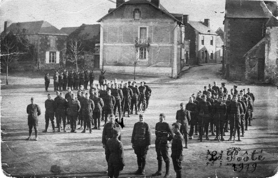Black and white photo of Soldiers in formation in opening of village
