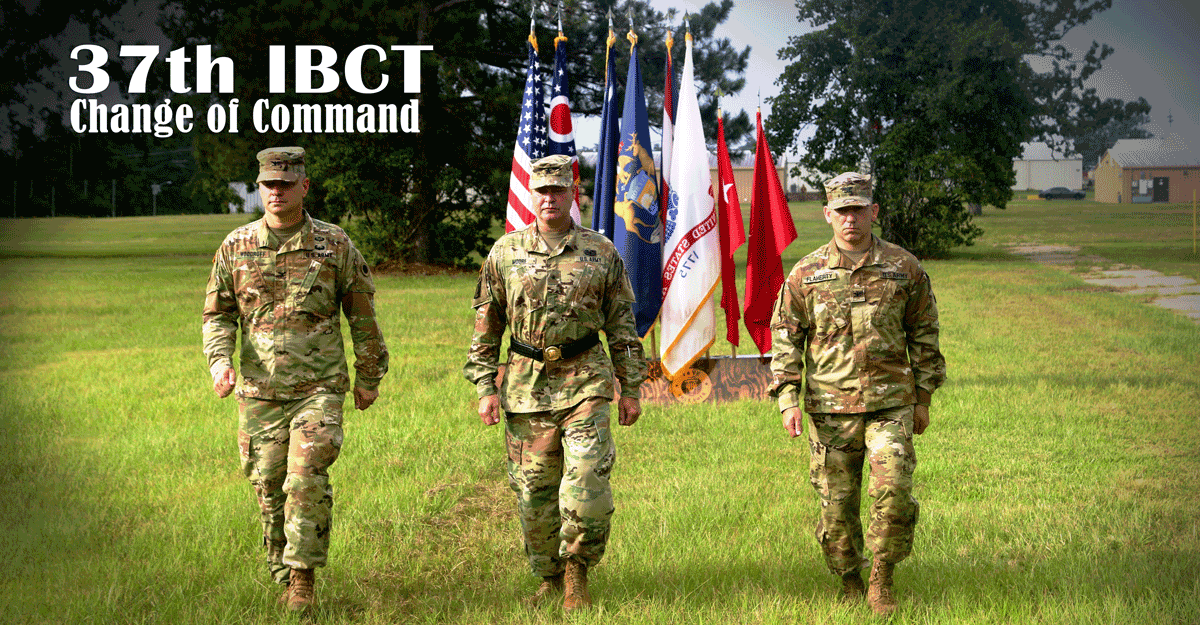 3 Commanders walking in formation with flags in background.