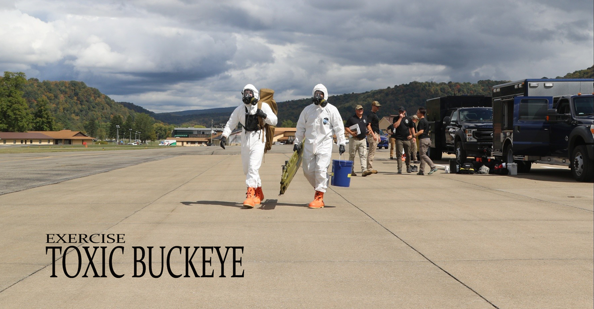 Two Soldiers in hazmat suits carry supplies