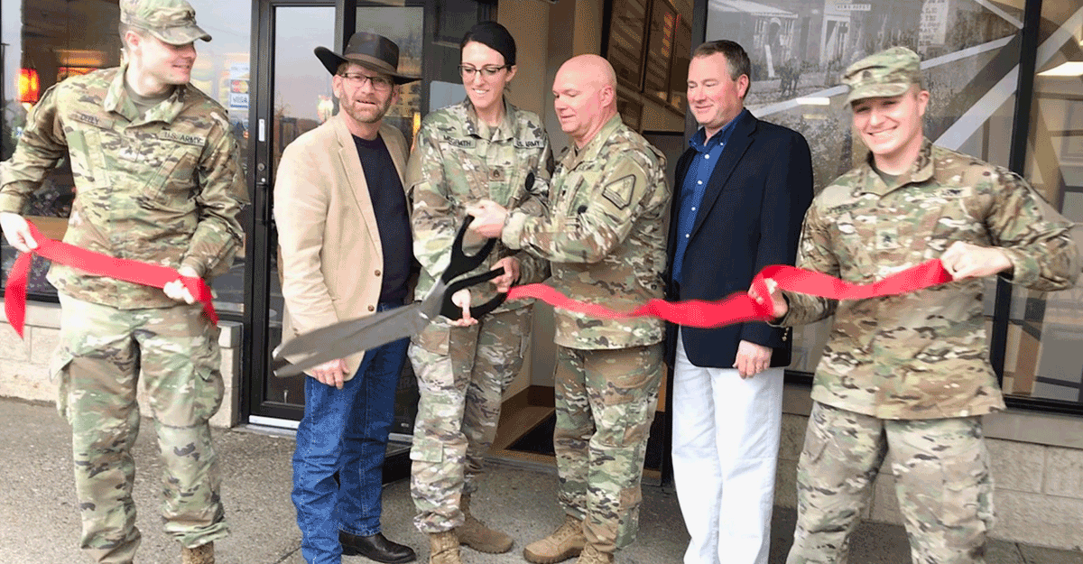 Soldiers cut red ribbon in front of new office.