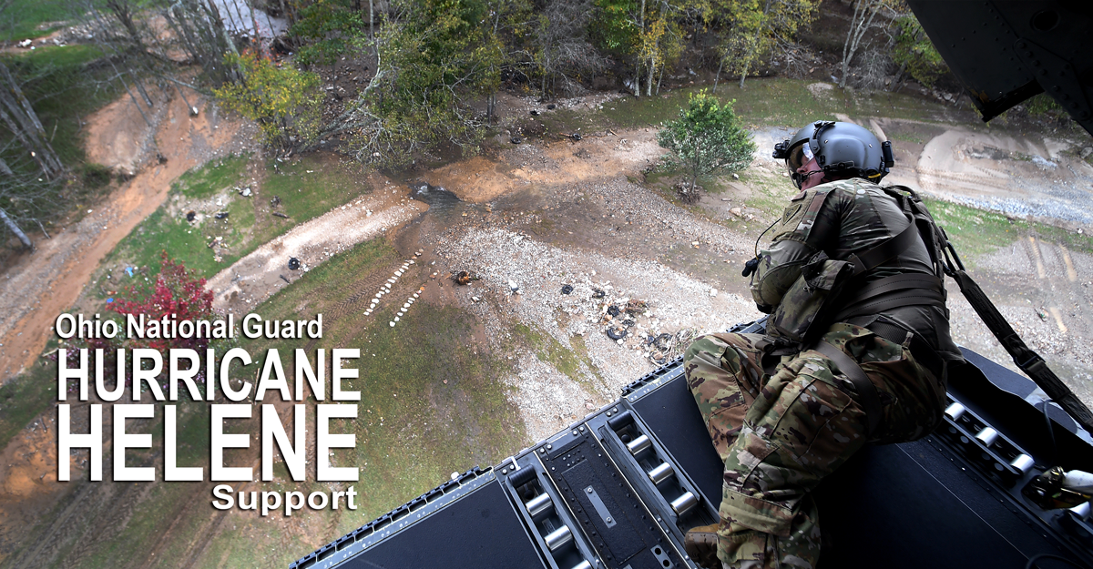 Airman looking down on flooding from the rear ramp of a CH-47 Chinook helicopter.