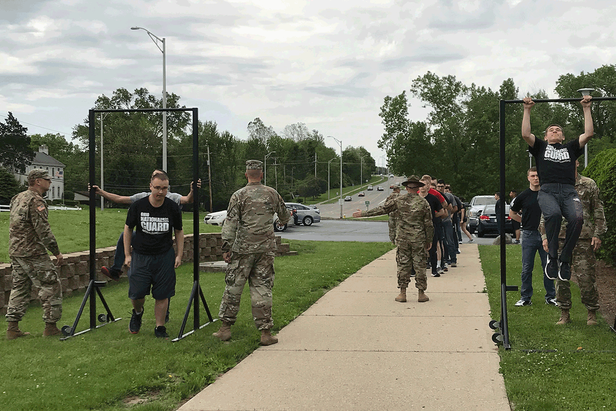 Soldiers conduct training with pull up bars along road with recruits.