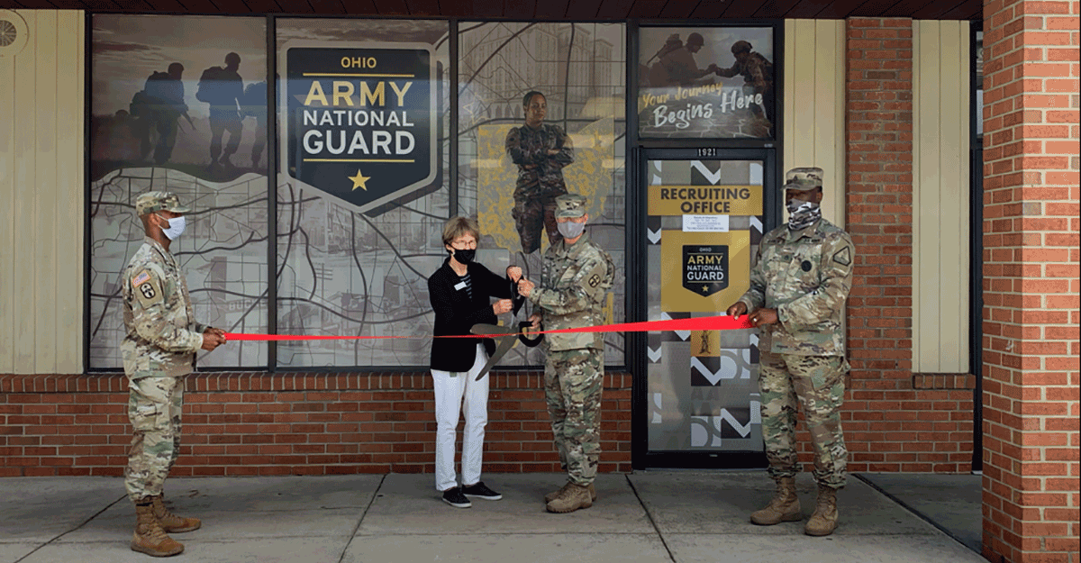 Guard Members with Councilwoman cut a llarge red ribbon at ARMY recruiting office storefront.