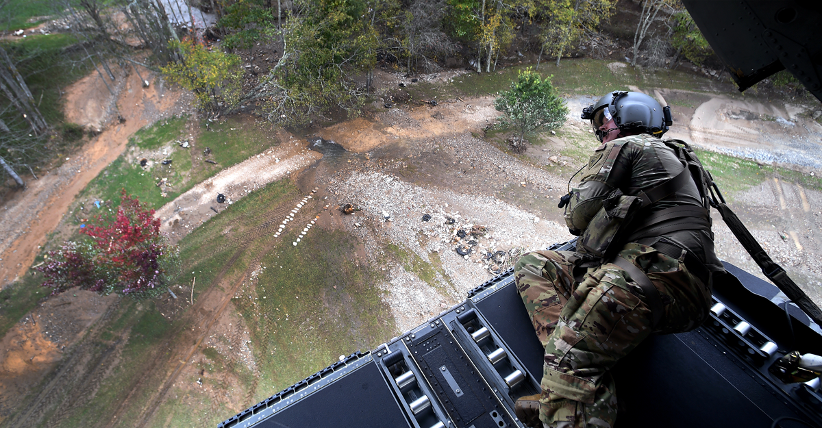 Airman looking down on flooding from the rear ramp of a CH-47 Chinook helicopter.