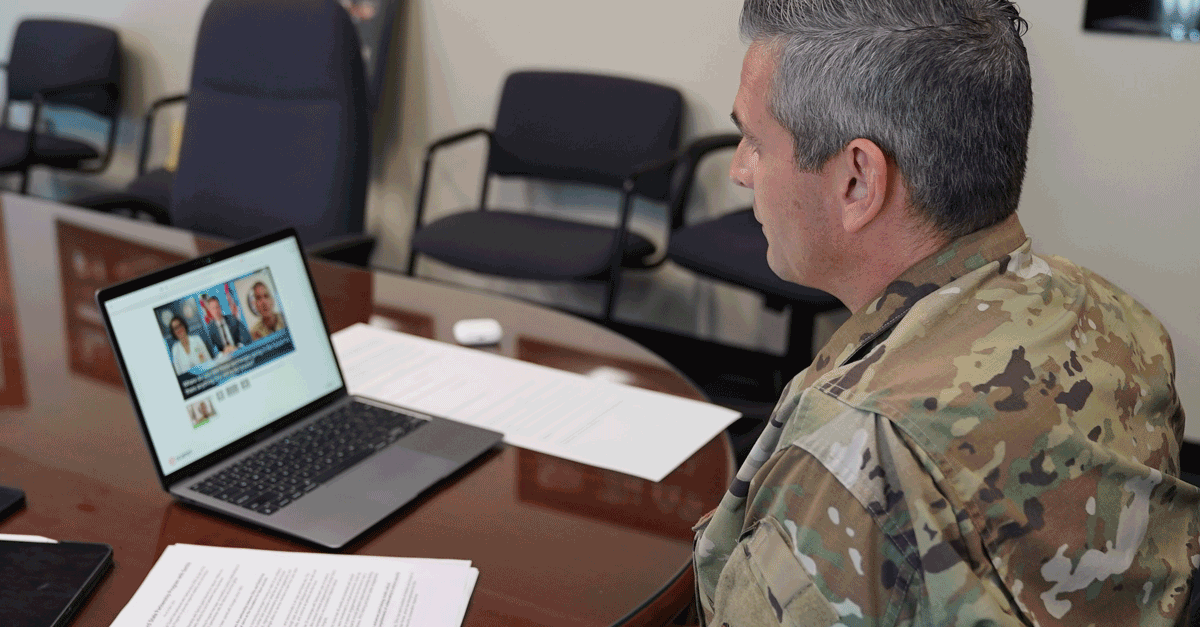 Soldier watches virtual meeting on laptop.